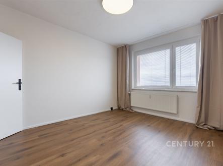 Prázdný pokoj s parketovou podlahou, velkým oknem a moderní výzdobou, ideální pro vytvoření světlého obytného prostoru