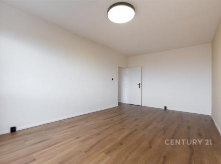 Prázdný pokoj s moderní parketovou podlahou, bílými stěnami a výrazným stropním svítidlem, ideální pro přizpůsobení osobním potřebám.