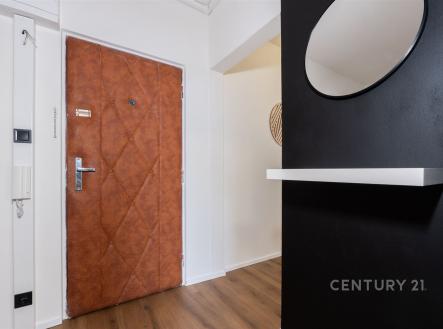 Vstupní chodba s dřevěnou podlahou, moderní černou stěnou a kulatým zrcadlem, dveře s koženým čalouněním, stylový interiér.