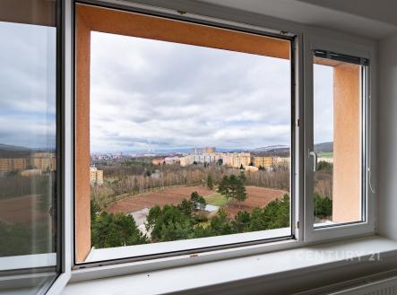 Světlý obývací pokoj s velkými okny, parketová podlaha, moderní výhled na město a zeleň, skvělá investiční příležitost.