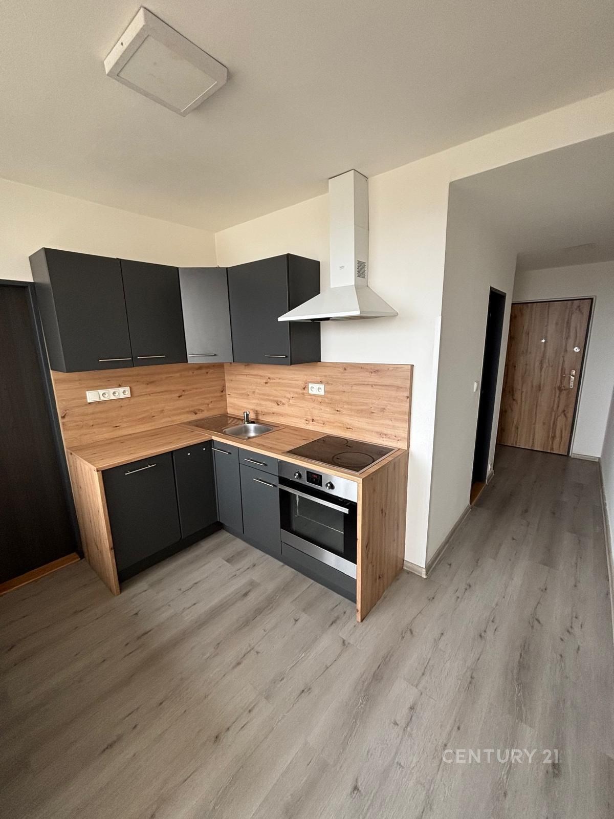 Moderní kuchyň s laminátovou podlahou, tmavými skříňkami a dřevěným obkladem. Vybavená sporákem a digestoří, moderní design.