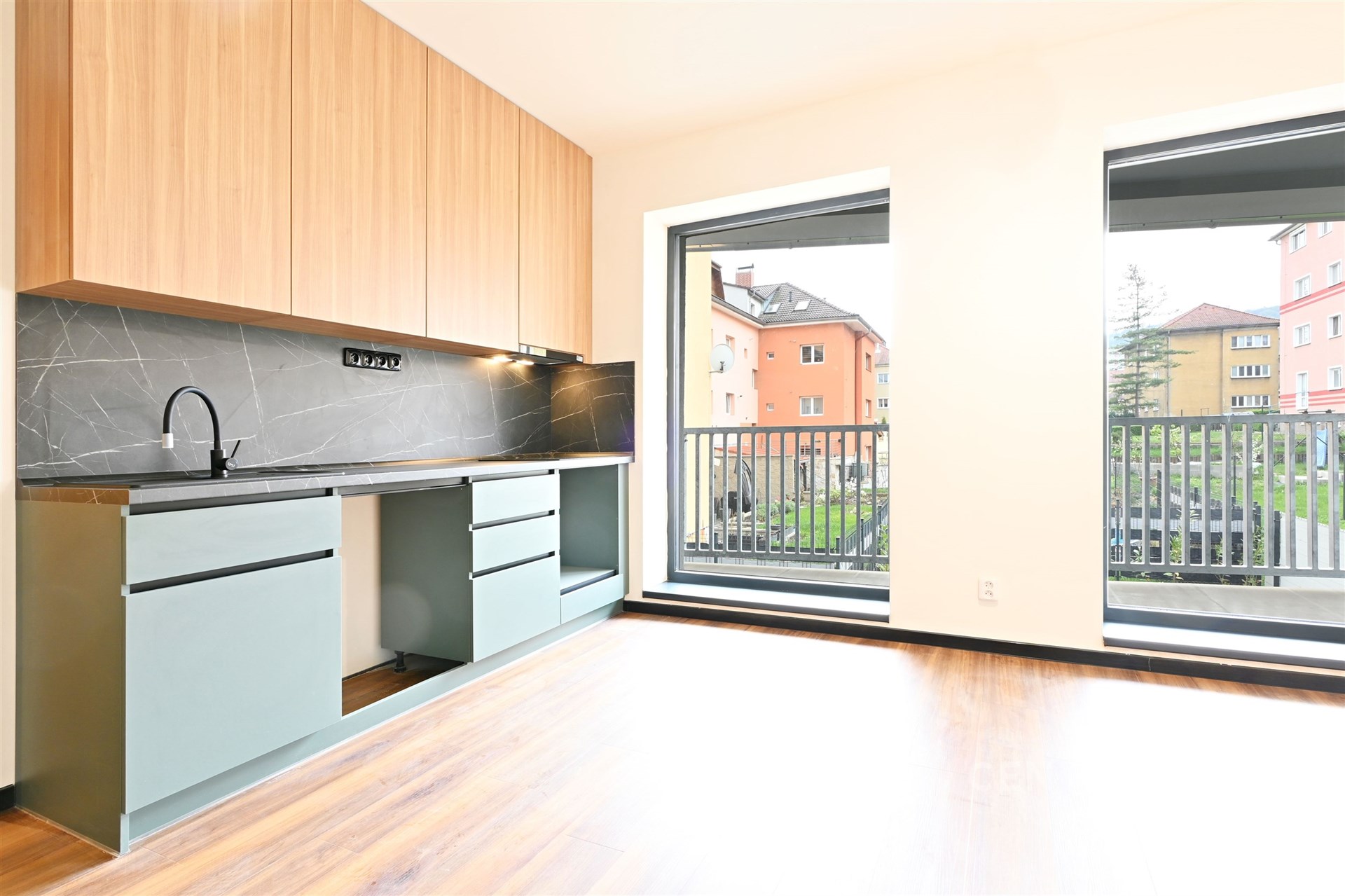 Moderní kuchyň s parketovou podlahou, vestavěnými skříněmi a velkými okny prosvětlujícími prostor.