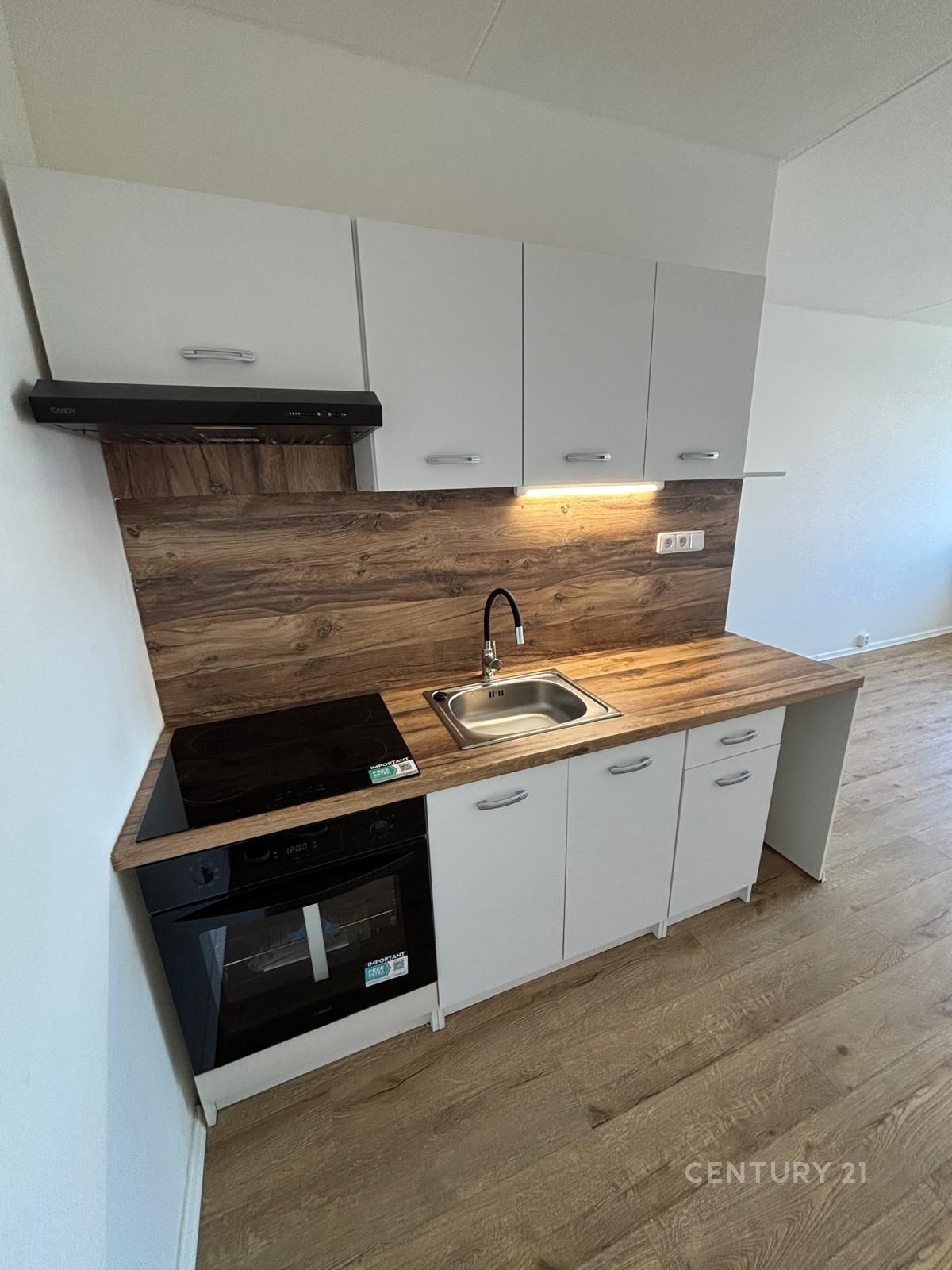 Moderní kuchyň s dřevěnou pracovní deskou, vestavěnými skříněmi a parketovou podlahou nabízí praktické a stylové řešení pro vaření.