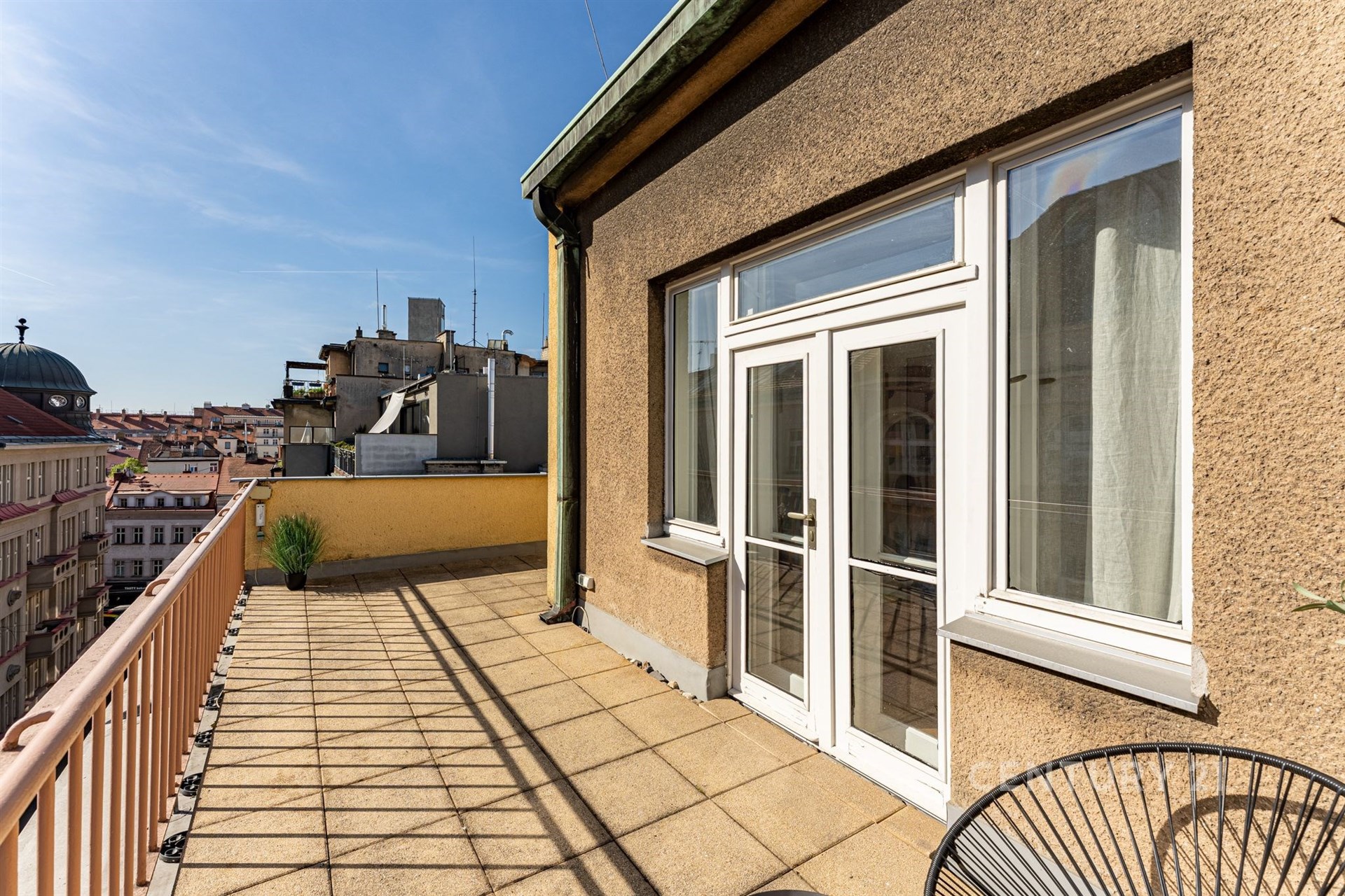 Velká terasa s dlažbou a velkými okny, nabízí krásný výhled na městskou panoramu, ideální pro moderní bydlení v centru města.