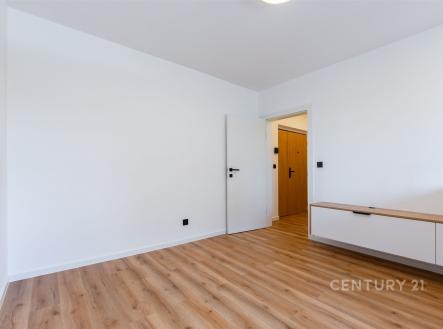 Světlý obývací pokoj s parketovou podlahou, moderní úložnou skříní a bílými stěnami, ideální pro stylové bydlení.