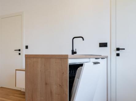 Moderní kuchyň s parketovou podlahou a světlým dřevem, vybavená vestavěnou myčkou a minimalistickým designem.