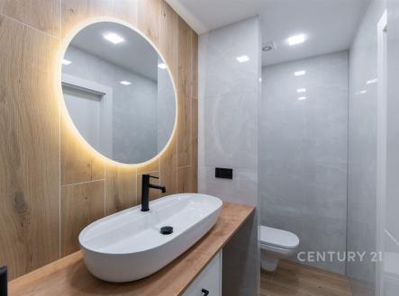 Moderní koupelna s dřevěným obkladem, oválné zrcadlo s LED osvětlením, světlé dlaždice a elegantní umyvadlo تعزيز منزلكم.