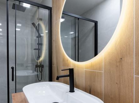 Moderní koupelna, dřevěný obklad, skleněný sprchový kout, oválné zrcadlo s LED osvětlením, elegantní černé vodovodní baterie