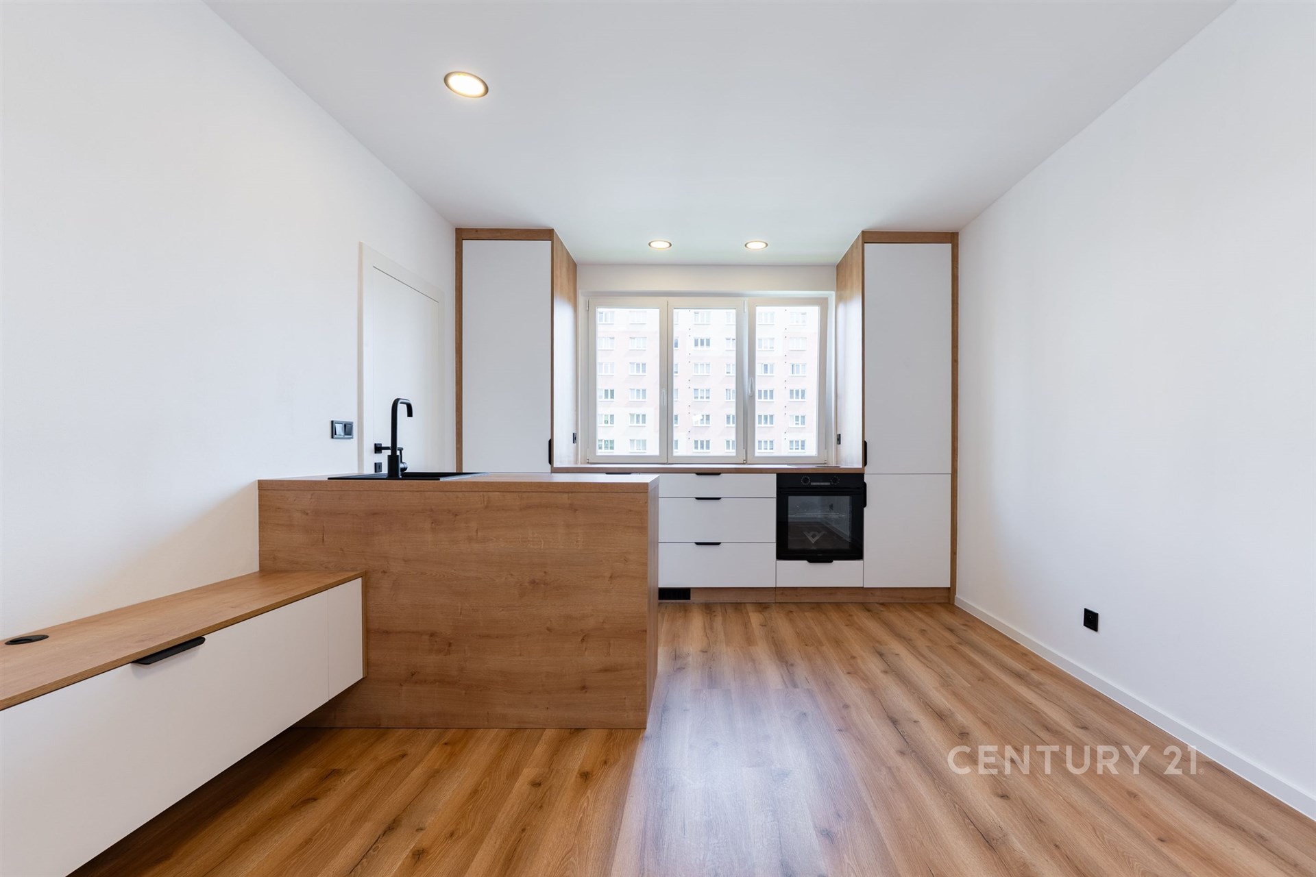 Moderní kuchyň s parketovou podlahou, velká okna poskytující dostatek světla, vestavěné skříně a minimalistický design