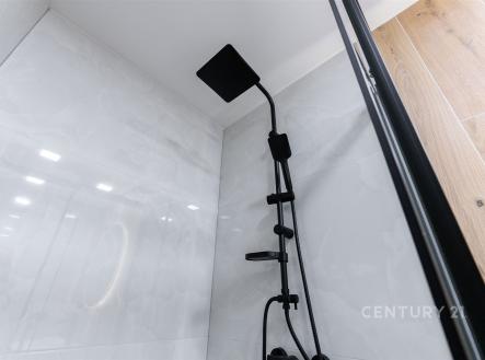 Koupelna s moderním černým sprchovým setem, lesklé dlaždice a elegantní dřevěné obložení vytváří stylový a nový interiér