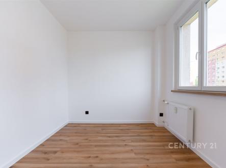 Světlý pokoj s dřevěnou podlahou a velkými okny, bílými stěnami a moderním vytápěním, ideální pro flexibilní využití.