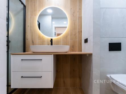 Moderní koupelna s dřevěnými obklady, vestavné umyvadlo a kulaté osvětlené zrcadlo, elegantní minimalistický design