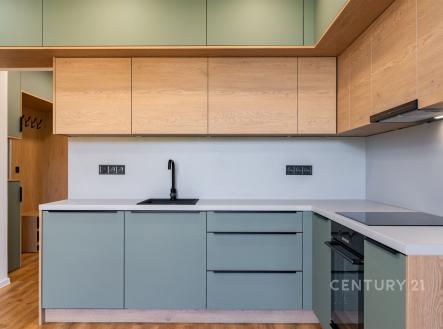 Moderní kuchyň s dřevěnými prvky, světlá parketová podlaha a vestavěné skříně, minimalistický design a integrované spotřebiče.