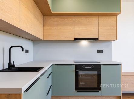 Moderní kuchyň s dřevěnými skříňkami, vestavěným spotřebičem a světlou pracovní deskou, minimalistický design a čisté linie.