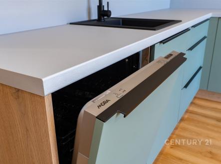 Moderní kuchyň s vestavěnou myčkou, dřevěná podlaha, minimalistické úchyty, světlé povrchy, elegantní dřez s černou baterií
