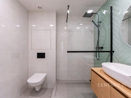 Moderní koupelna, světlé dlaždice, prosklený sprchový kout, dřevěný nábytek, závěsné WC, elegantní design.