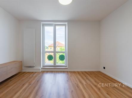 Světlý obývací pokoj s parketovou podlahou, velká okna a moderní minimalistický design, vytváří světlou a příjemnou atmosféru.