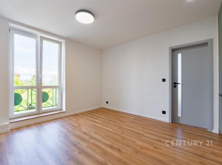 Světlý obývací pokoj s parketovou podlahou, velká okna poskytují dostatek denního světla, moderní design s neutrálními barvami.
