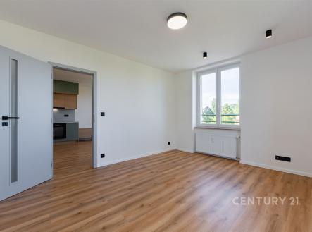 Světlý obývací pokoj s parketovou podlahou, velká okna poskytují dostatek přirozeného světla, moderní design v rekonstruovaném bytě.