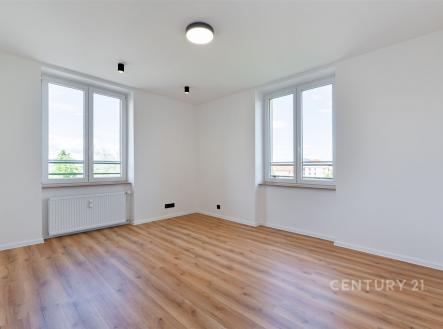 Světlý obývací pokoj s parketovou podlahou, velkými okny a moderním osvětlením v rekonstruovaném bytě.