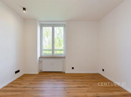 Prázdná místnost s parketovou podlahou, velkým oknem a moderním designem. Světlý interiér vytváří pocit prostoru a elegance.