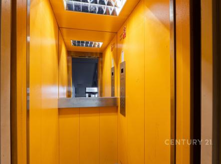 Prázdný výtah s výraznými oranžovými stěnami a kovovými doplňky, moderní osvětlení, bezpečnostní prvky, ideální pro residenční budovu.