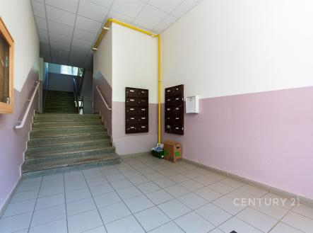 Vstupní hala bytového domu s dlažbou, poštovními schránkami a schodištěm, které vede do vyšších pater, čisté a světlé prostředí.
