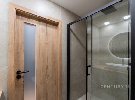 Moderní koupelna s elegantní dlažbou, sprchovým koutem s prosklenými dveřmi a dřevěným obkladem, vytvářející minimalistický vzhled.