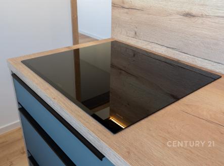 Moderní kuchyň s indukční deskou, dřevěná pracovní deska a vestavěné skříně, minimalistický styl.