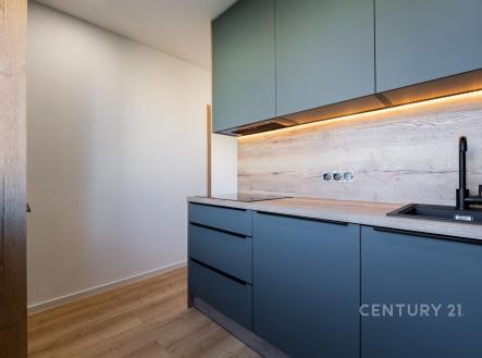 Moderní kuchyň s dřevěnou podlahou, vestavěné skříně, minimalistický design, LED osvětlení pod skříněmi, matné povrchy, elegantní černý dřez.