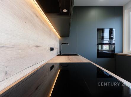 Moderní kuchyň s dřevěnou pracovní plochou, vestavěnými spotřebiči a LED osvětlením vytváří elegantní a funkční prostor.