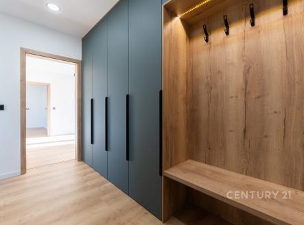 Vstupní chodba s moderními vestavěnými skříněmi, dřevěnými obklady a parketovou podlahou, poskytující světlý a elegantní vzhled.