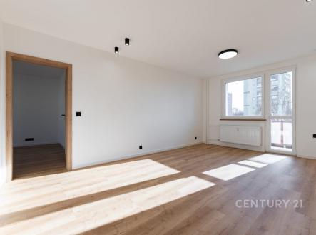 Světlý obývací pokoj s velkými okny, moderní parketovou podlahou a bílými stěnami, ideální pro útulný interiér.