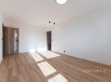 Světlý obývací pokoj s parketovou podlahou, velká okna poskytují dostatek přirozeného světla, moderní styl a neutrální barvy stěn.