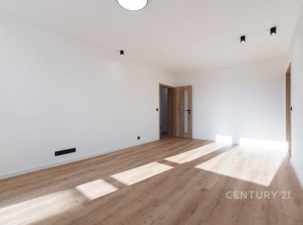 Světlý obývací pokoj s parketovou podlahou, moderní osvětlení, velká okna poskytující dostatek přirozeného světla, nedávno rekonstruovaný prostor.
