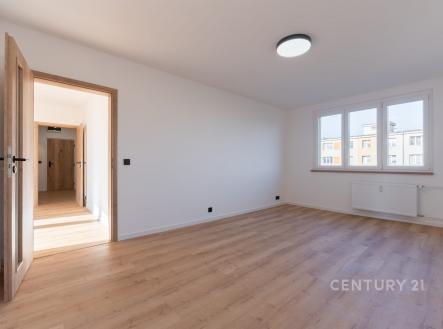 Světlý obývací pokoj s dřevěnou podlahou, velkými okny a moderním osvětlením, ideální pro útulné bydlení v rekonstruovaném bytě.