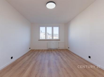 Světlý pokoj s parketovou podlahou a velkými okny, nabízející moderní atmosféru a výhled na okolní krajinu.