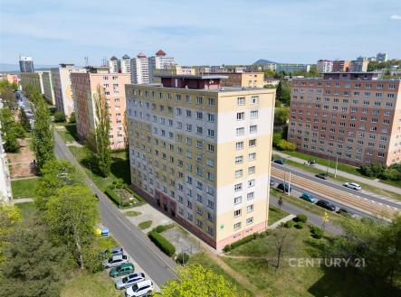 Venkovní pohled na panelový bytový dům v Praze s rekonstruovanou fasádou, parkovacími místy a blízkostí tramvajové zastávky.