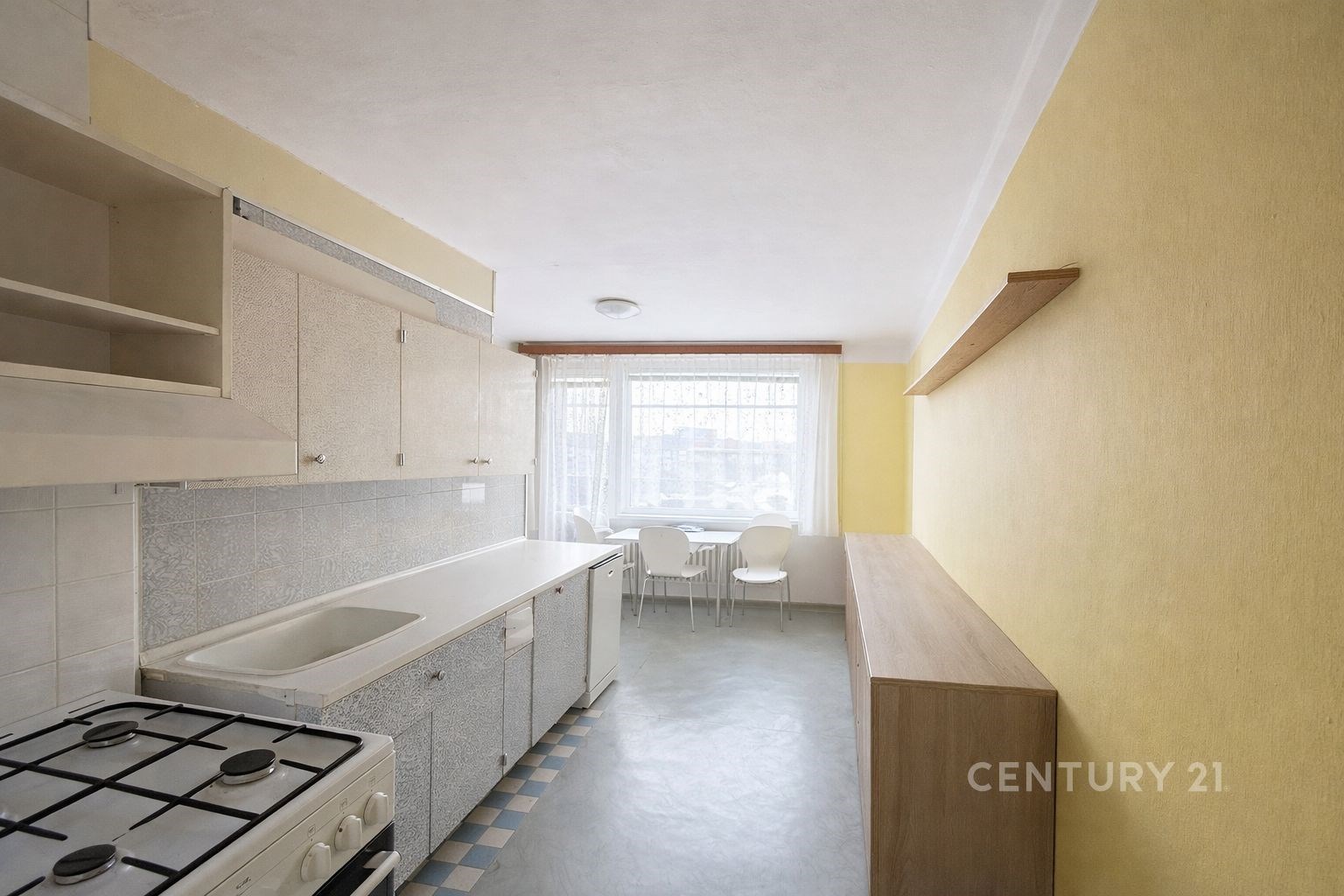 Kuchyně s linoleem a velkým oknem, světlé skříňky, prostorný jídelní kout, žluté stěny vytvářejí moderní a útulný prostor.