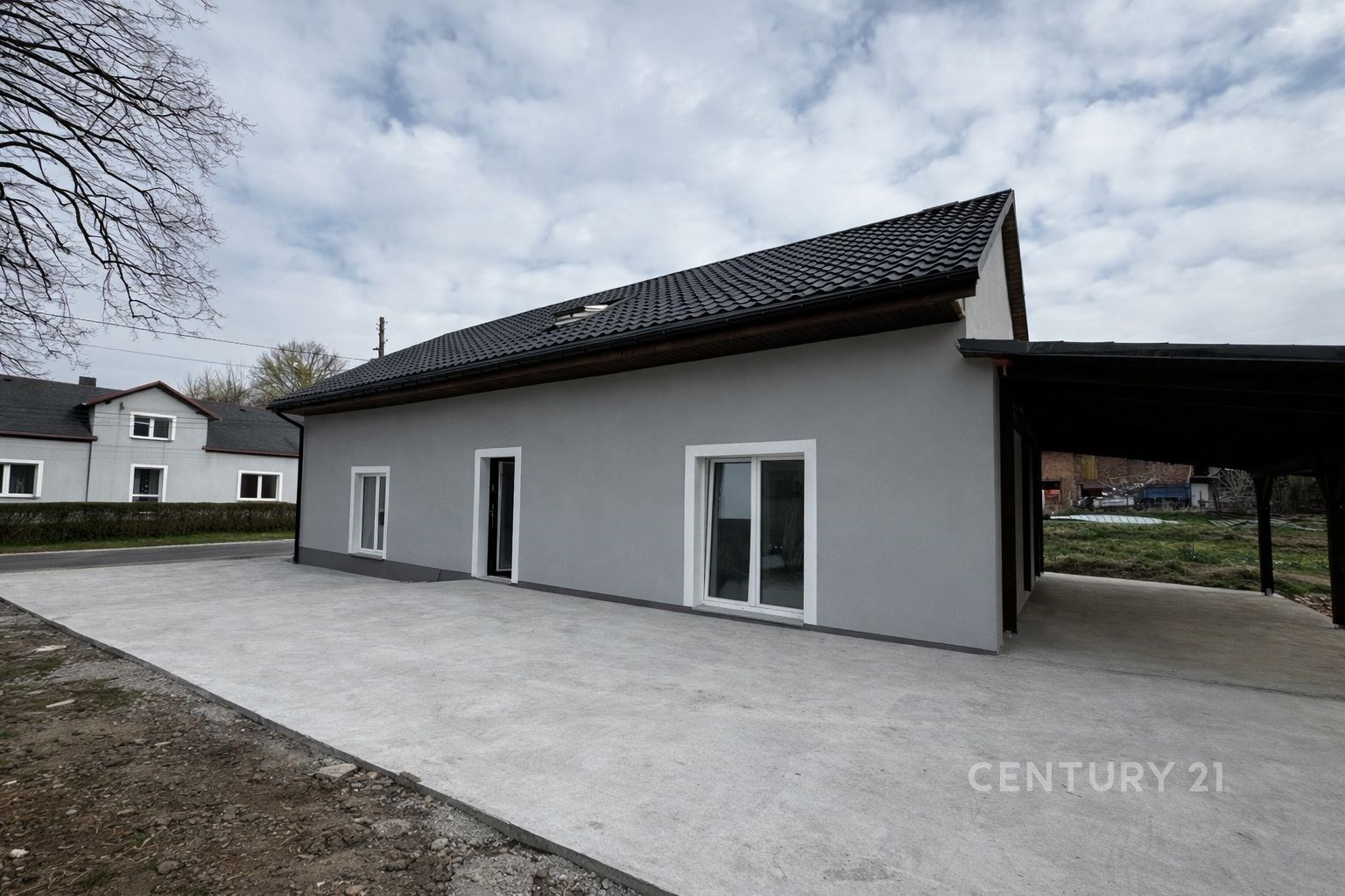 Moderní rodinný dům s šedou fasádou a velkými francouzskými okny, dlážděný prostor v klidné oblasti, vhodný pro pohodlné bydlení.