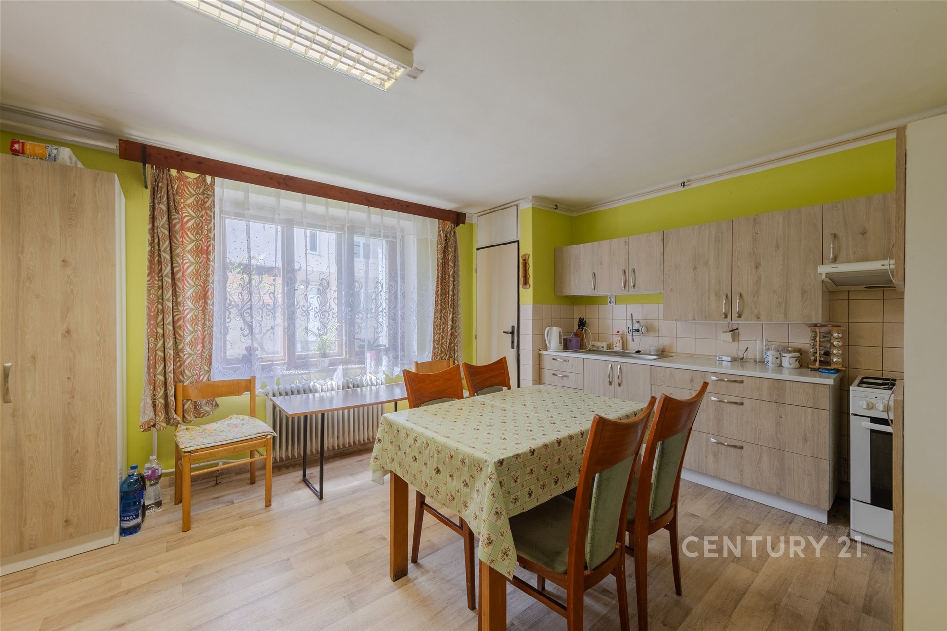 Prostorná kuchyň s parketovou podlahou, vestavěnými skříněmi a velkými okny, které zajišťují světlé prostředí.