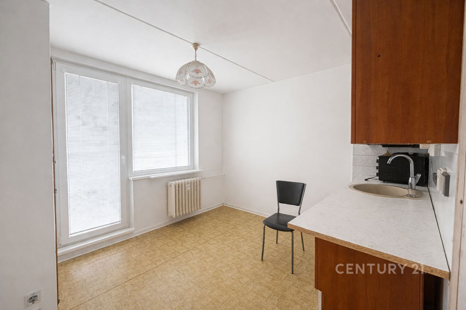 Světlá kuchyň s laminátovou podlahou, velkými okny a vestavěným radiátorem nabízí moderní prostor ideální pro rekonstrukci.