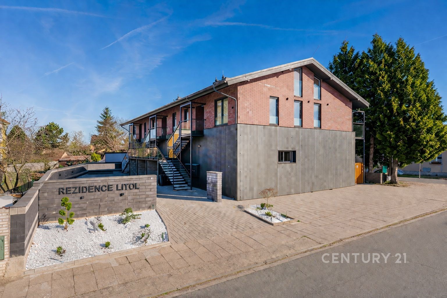 Rezidenční budova s moderní fasádou, velkými okny a cihlovým obkladem. Klidná lokalita s upraveným okolím a přístupovým chodníkem.