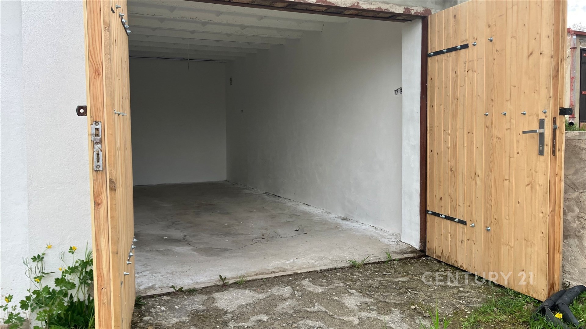 Prázdná garáž s betonovou podlahou a novými dřevěnými vraty, ideální pro parkování vozidla nebo skladovací účely.