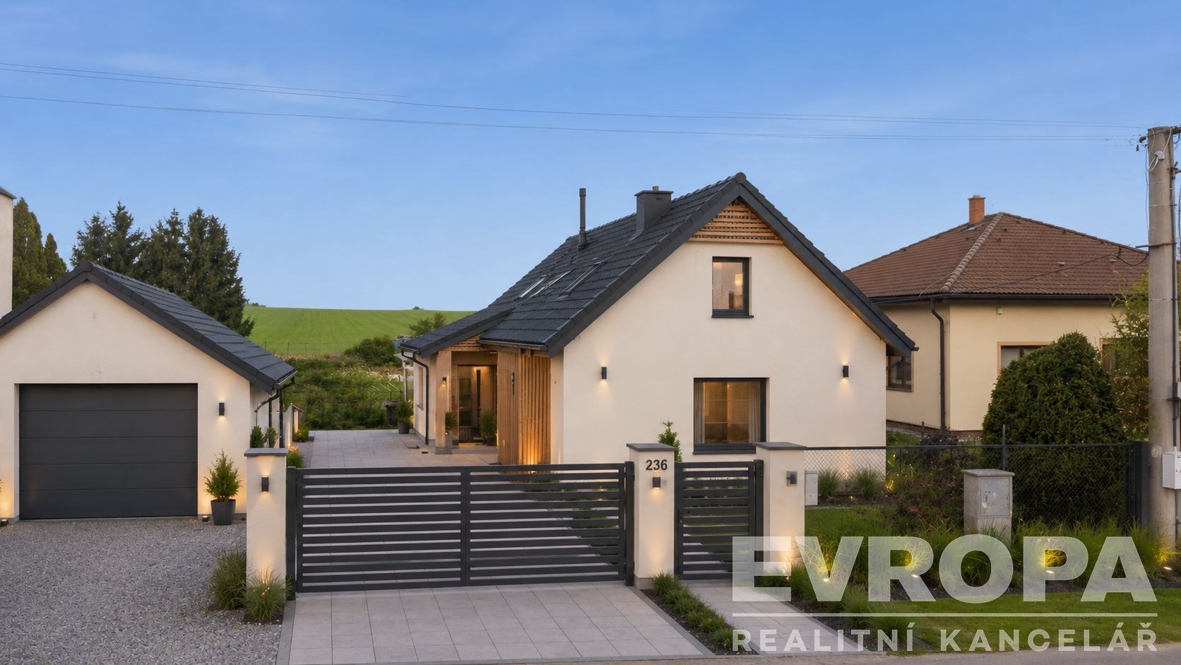 Moderní rodinný dům s elegantní fasádou, velká okna a upravená zahrada, nacházející se v klidné oblasti s garáží a dlážděným příjezdem.