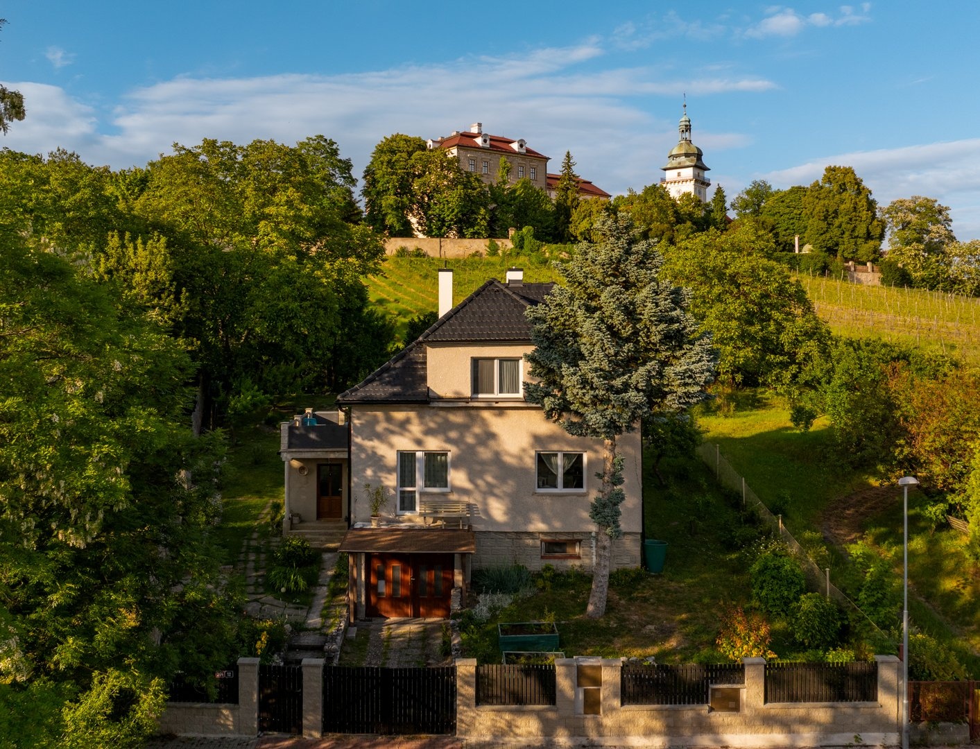 Pohled na dům z výšky z ulice, v pozadí zámek