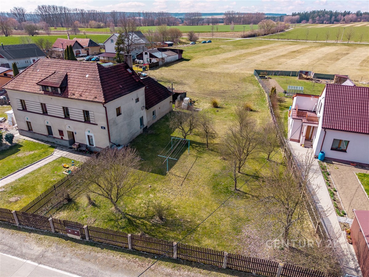 Prázdná zahrada s travnatým povrchem u rodinného domu, oplocená dřevěným plotem, ideální pro úpravu dle vlastních představ.