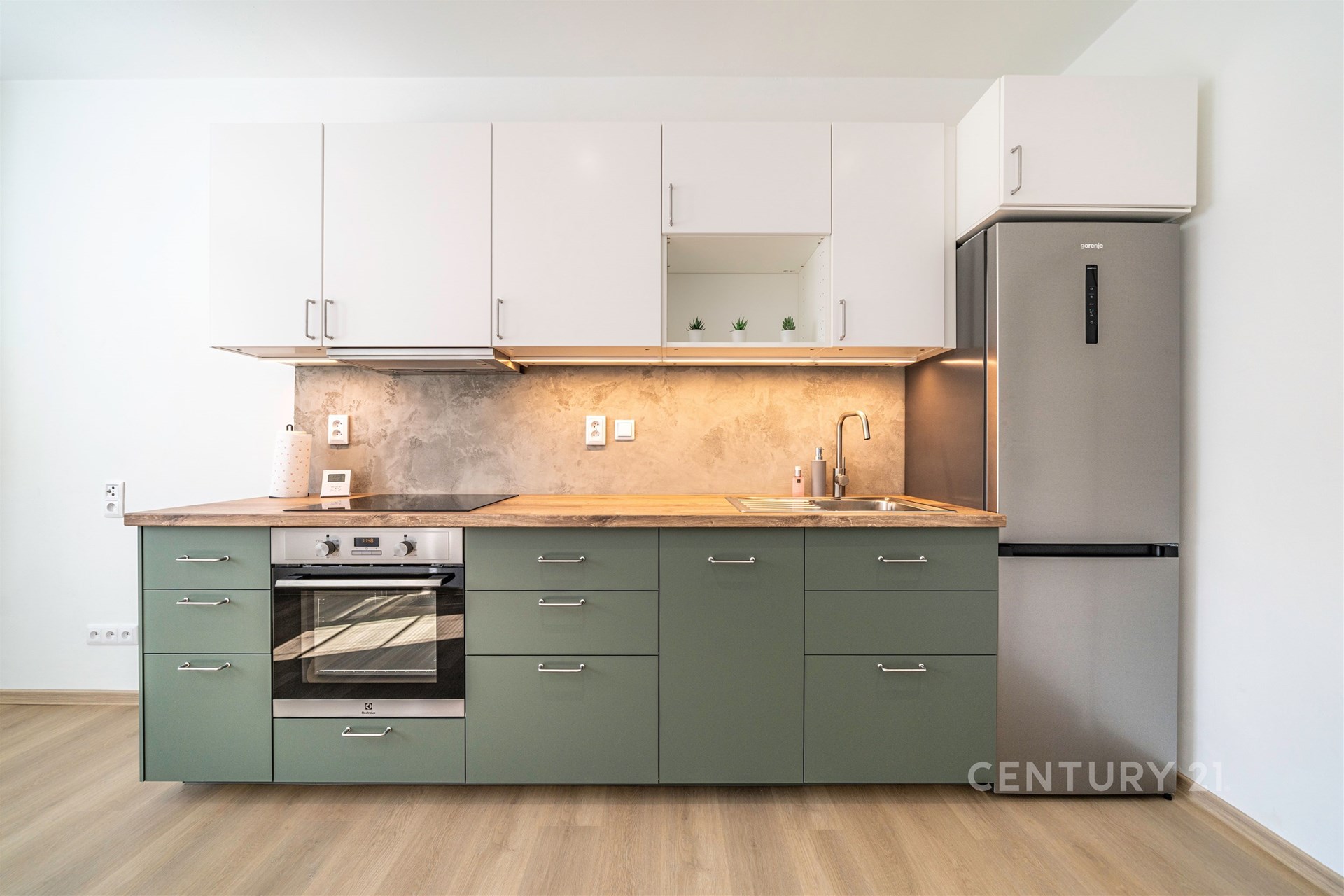 Moderní kuchyň s parketovou podlahou, zelenými skříněmi a nerezovou lednicí, zařízená pro sváteční vaření, zdůrazňuje světlý a funkční design.