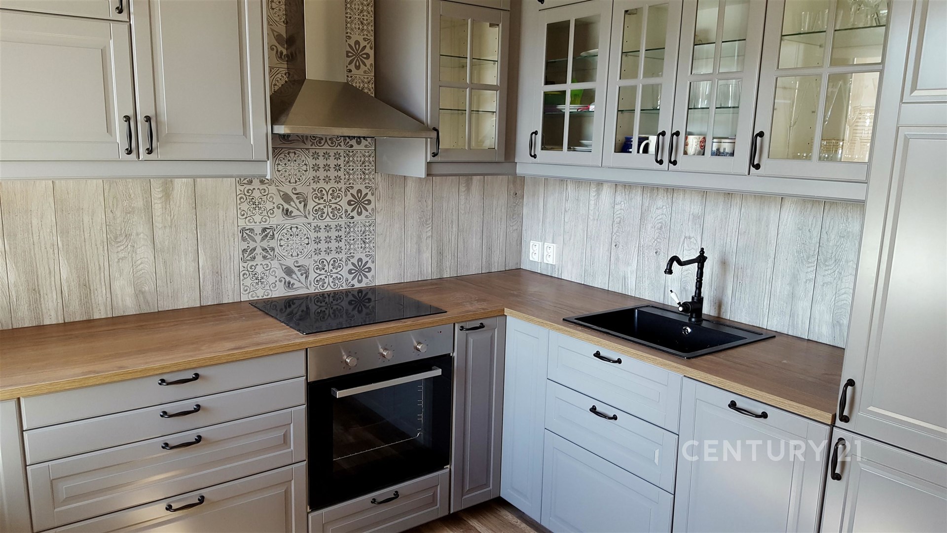 Stylová kuchyň s dřevěnou pracovní deskou a parketovou podlahou, moderní vestavěné spotřebiče, skleněné vitríny, dekorativní dlažba za sporákem.