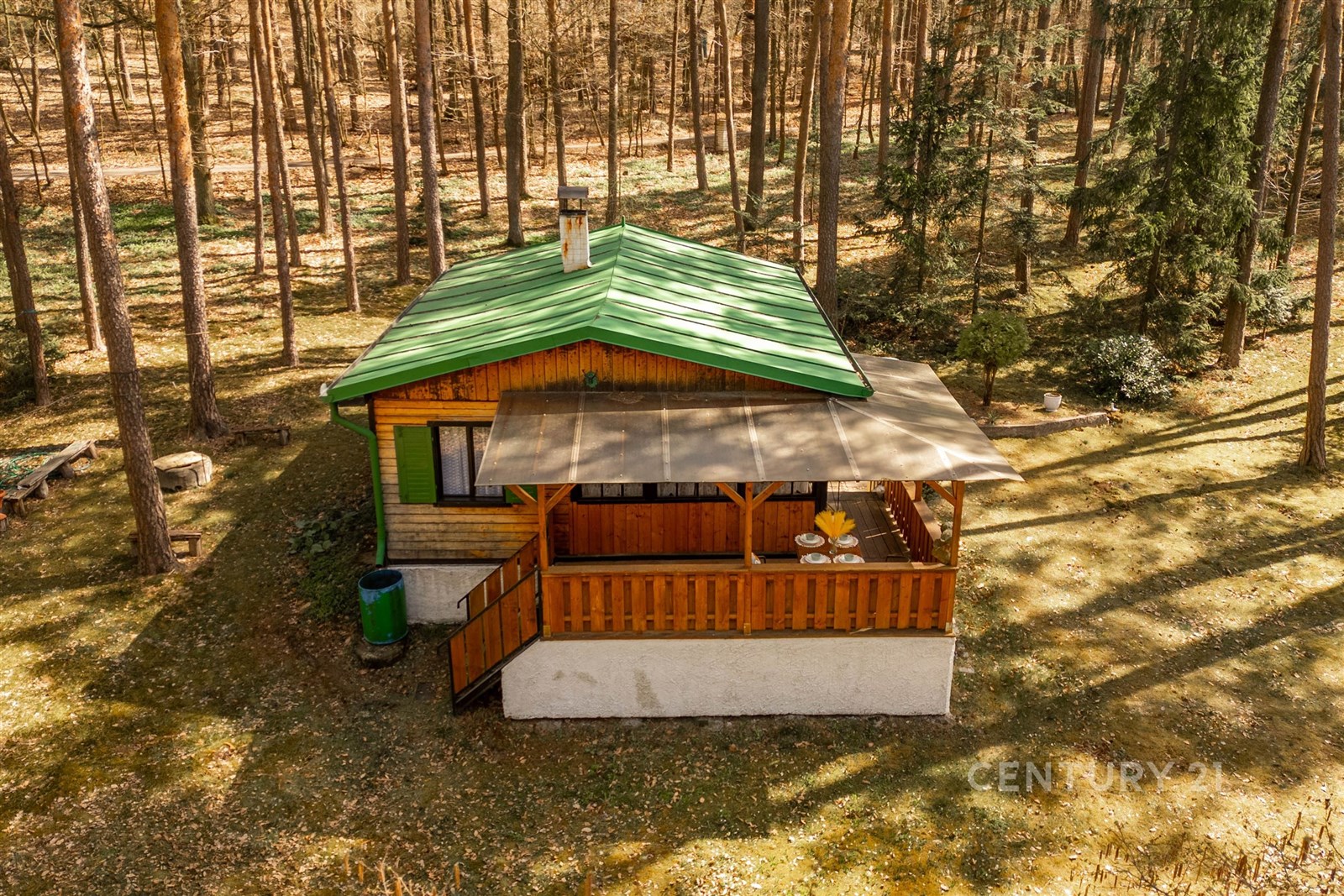 Dřevěná chata s terasou v lese, zelená střecha, klidná lokalita, vhodné pro rekreaci, obklopená stromy poskytující soukromí.